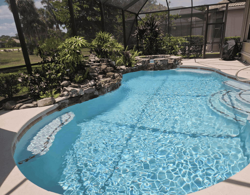 Crystal-clear freeform pool water with rock waterfall feature and freshly vacuumed interior by Pools USA in Port St. Lucie, FL.