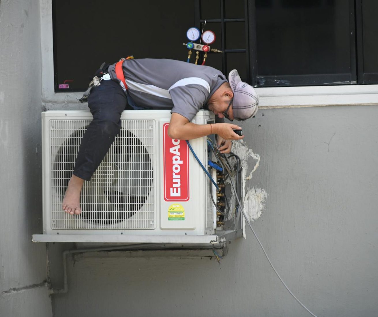 A technician skillfully repairing an outdoor air conditioning unit mounted on a building wall.